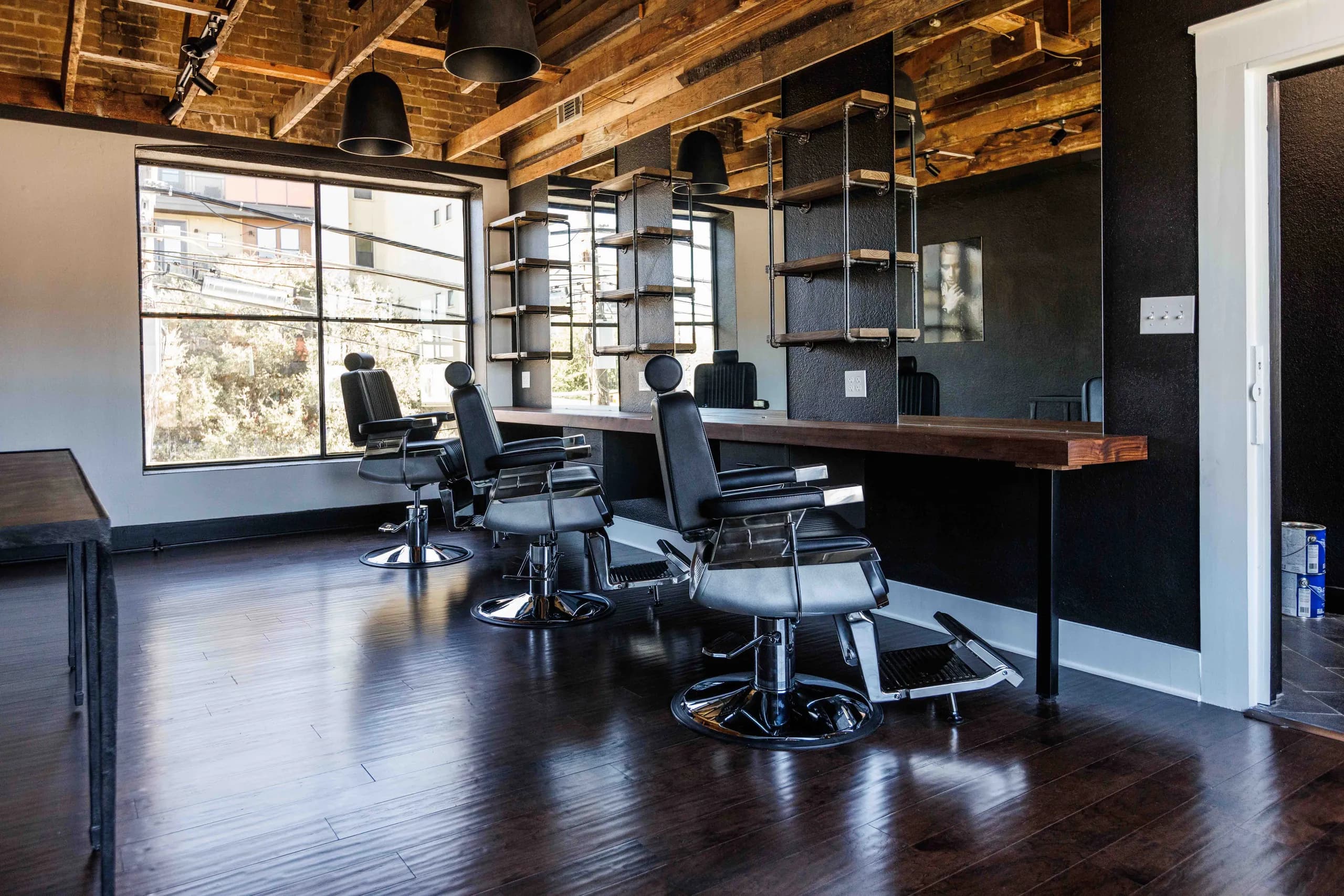 Barbershop with black chairs, a long counter, open shelving, and a patterned ceiling