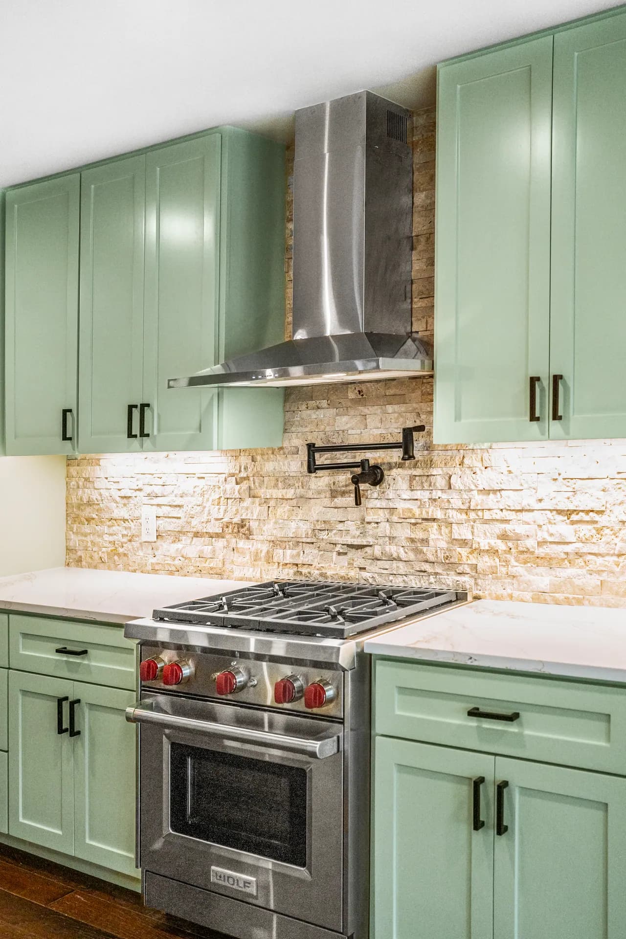 Green cabinetry, stone backsplash, and range in Domain’s Northwest Austin remodel