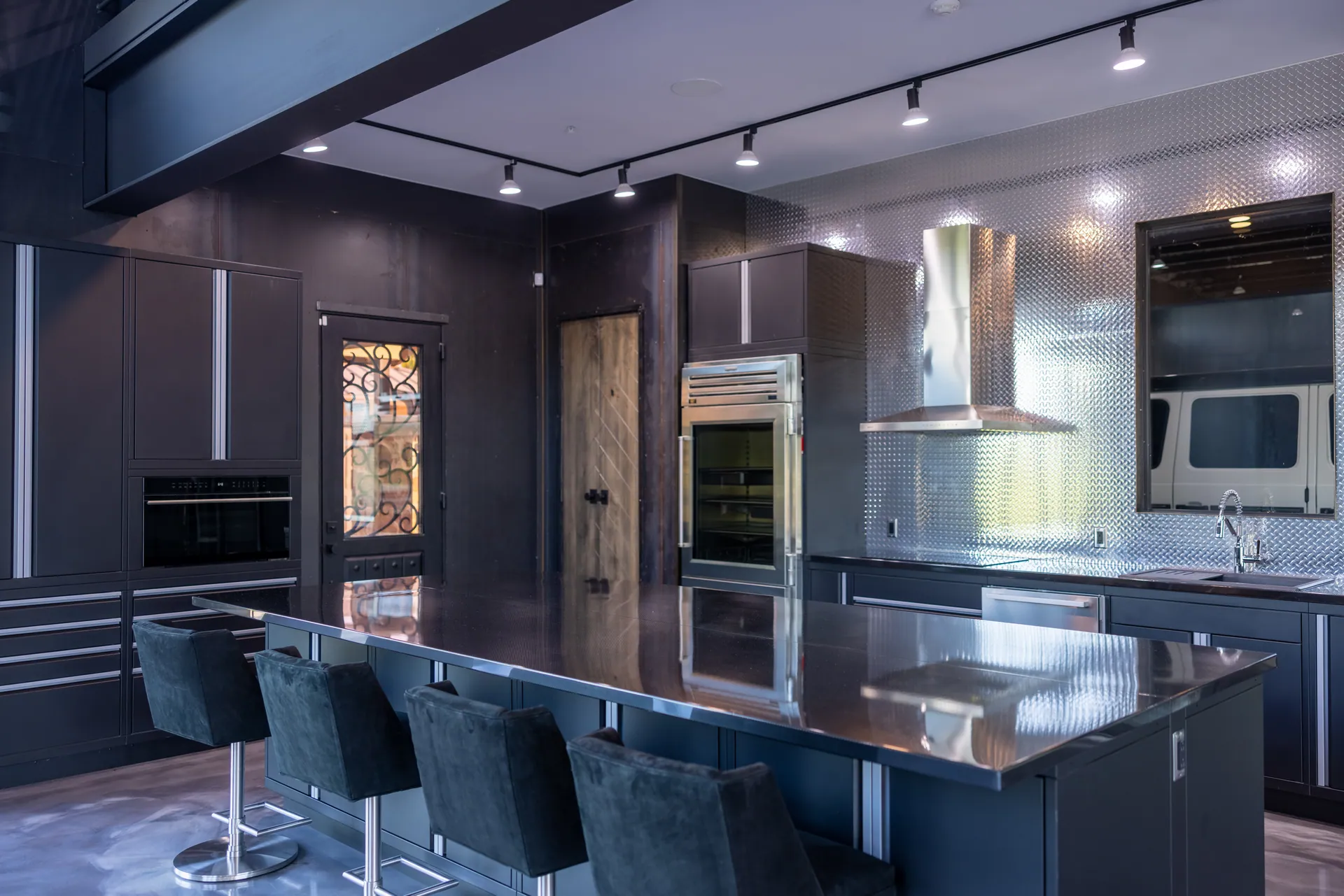 Dark kitchen cabinetry, metal backsplash, and counter seating beneath the mezzanine