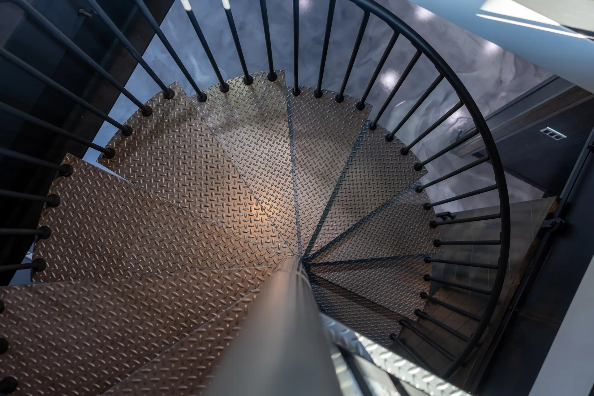 Spiral metal stair seen from above, with patterned treads and slender railings