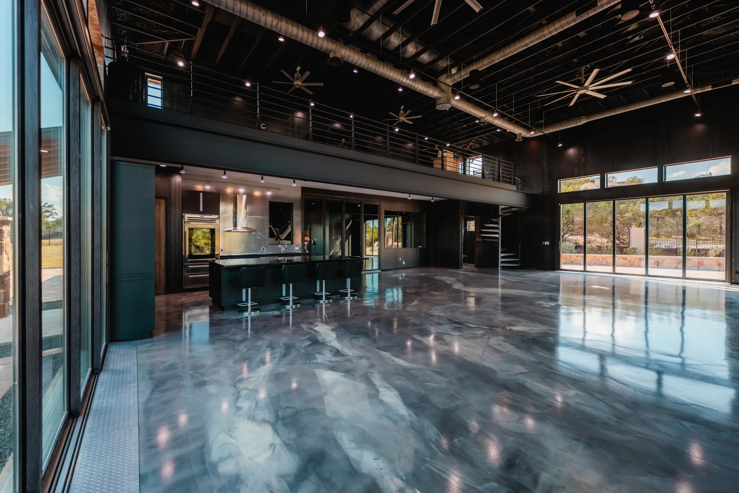 Double-height steel interior with mezzanine, dark kitchen, spiral stair, and reflective floor