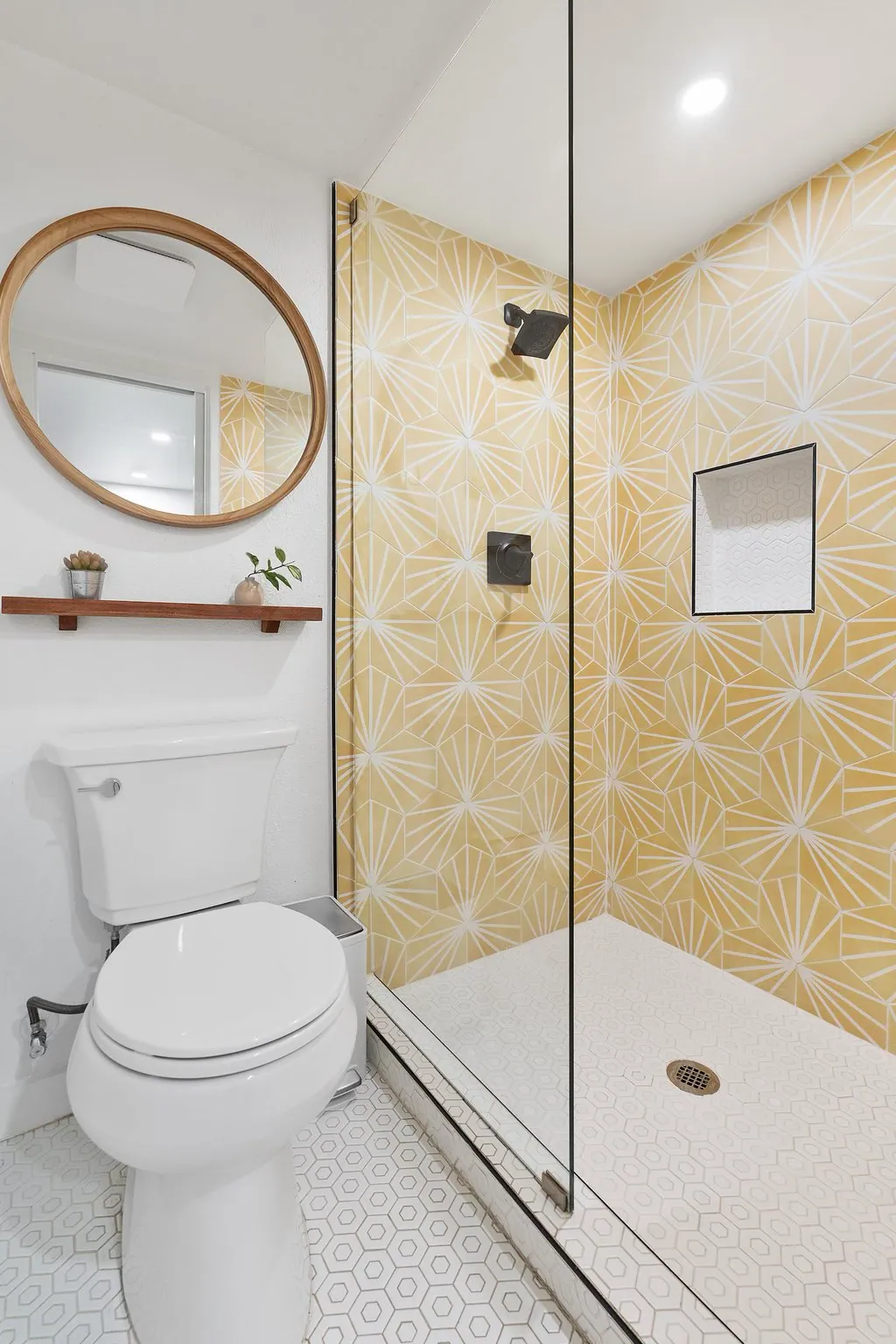 Yellow geometric shower tile, glass enclosure, and round wood-framed mirror in Domain’s Tuff Shed ADU