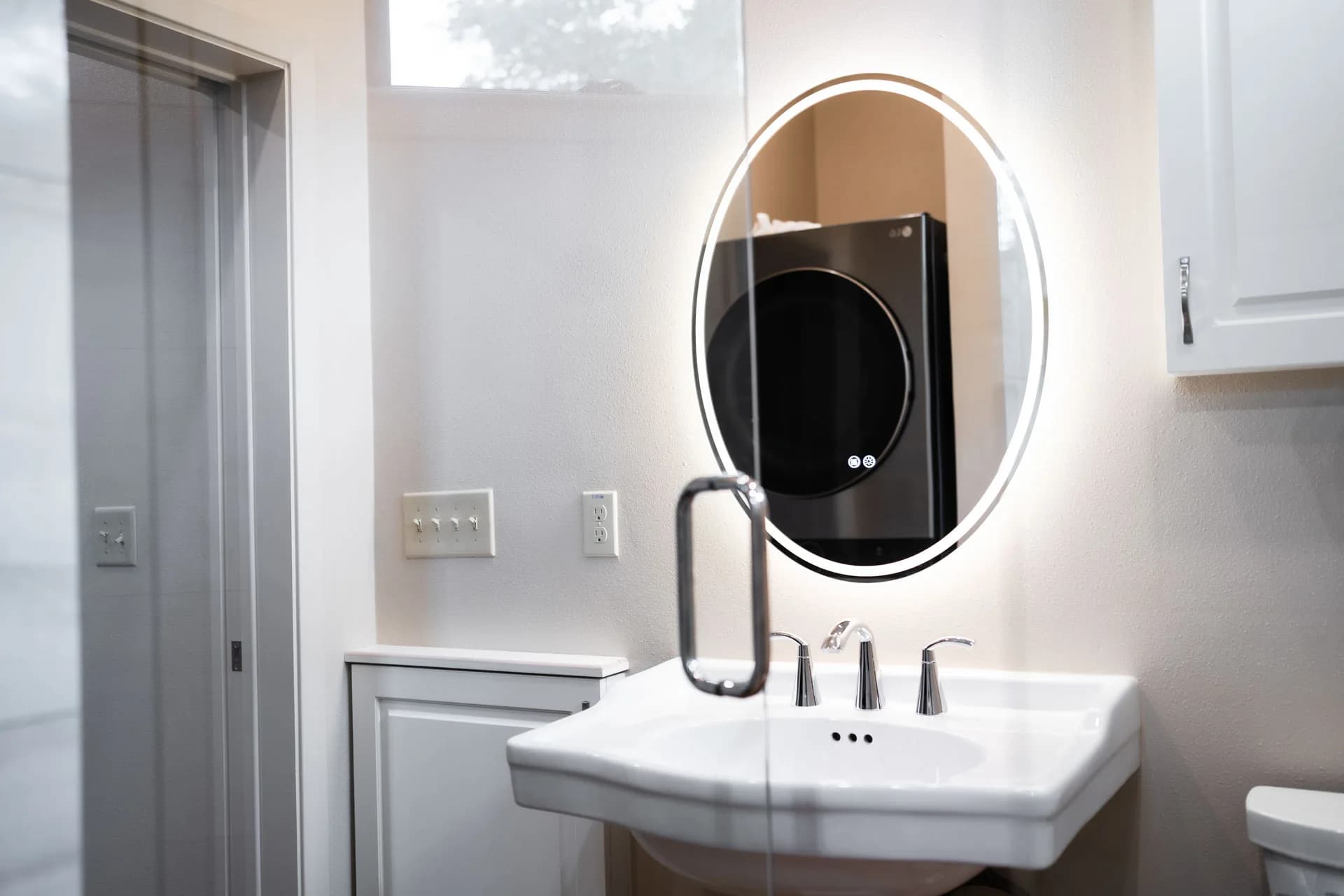 Illuminated oval mirror, vessel basin, and shower in Domain’s Tan Container ADU bathroom