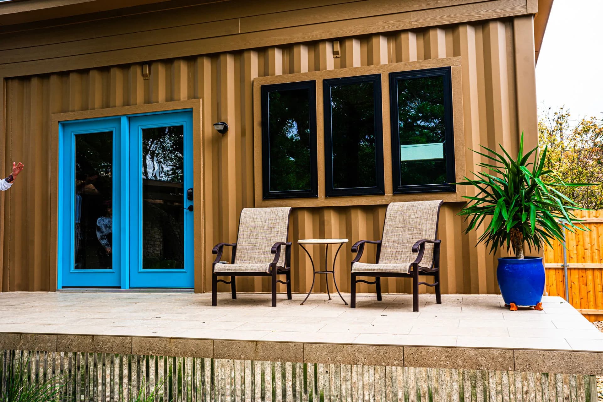 Blue doors, seating, and potted plants on the Tan Container ADU deck