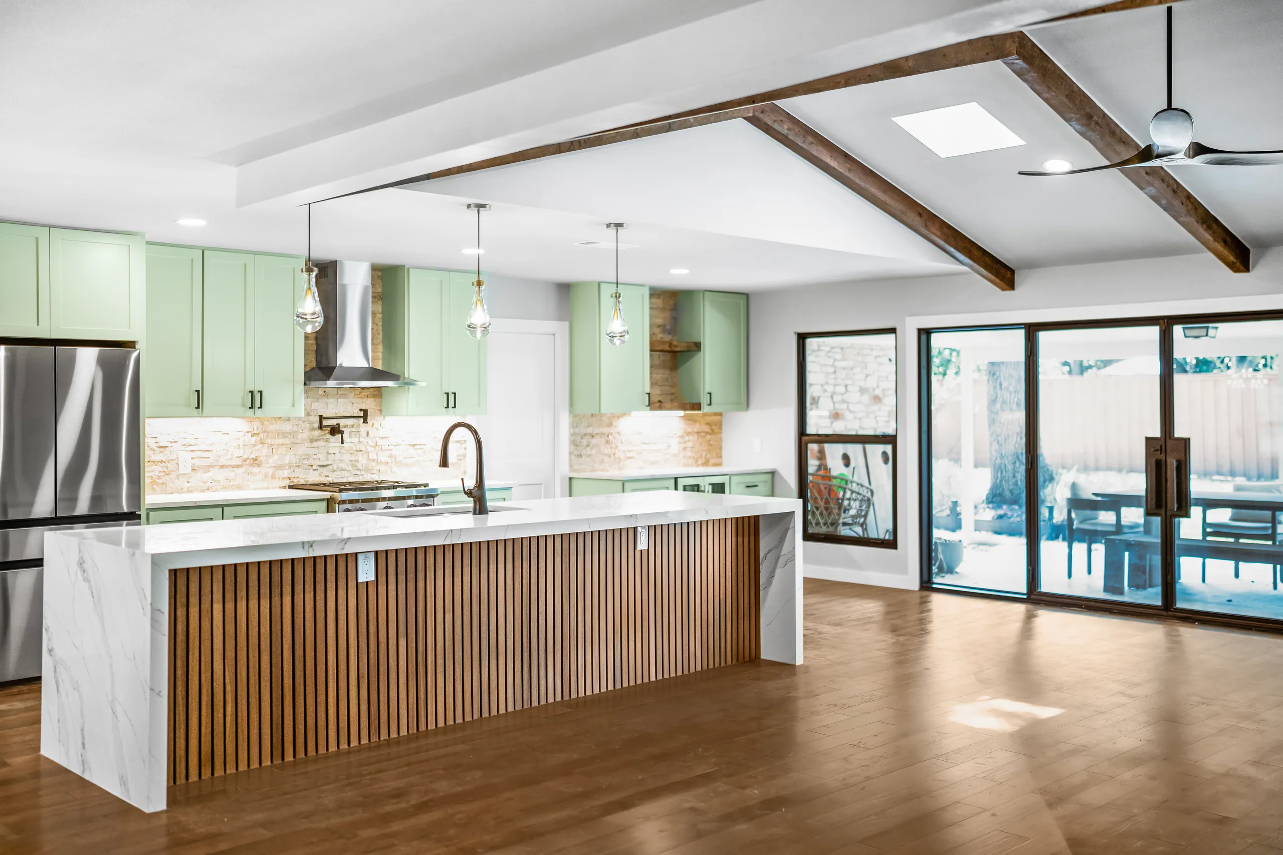 Quartz island, wood slat front, green cabinetry, and exposed beams in Domain’s Northwest Austin remodel
