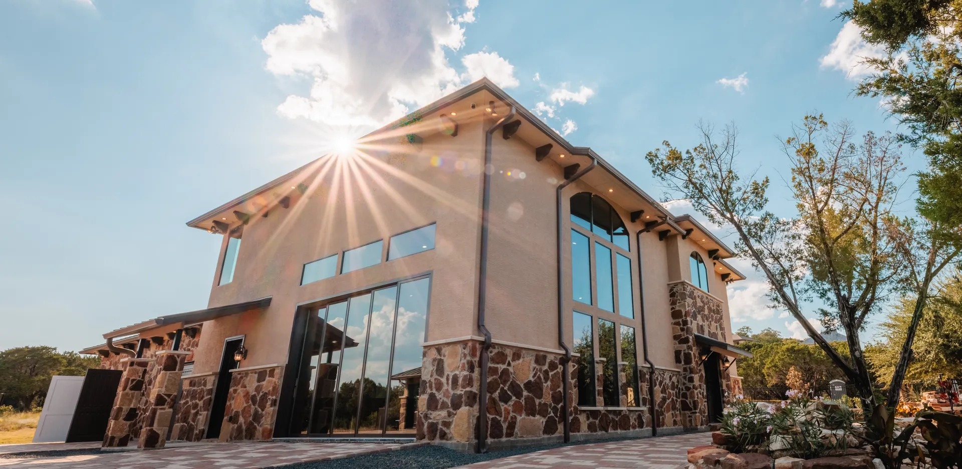Two-story building with tall arched glazing and exposed rafter tails, photographed against the sun